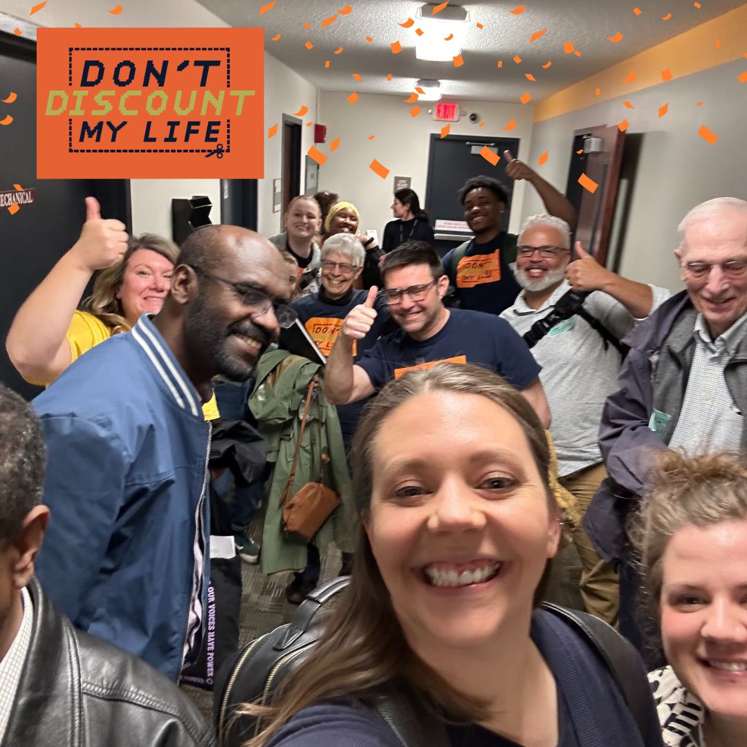 Selfie of a group of happy people in a hallway. Don't Discount My Life logo at top left.