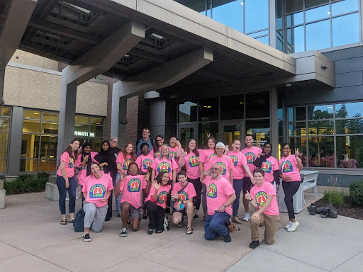 A group of 23 people wearing pink shirts smiling and posing in front of the Richfield Municipal Center.